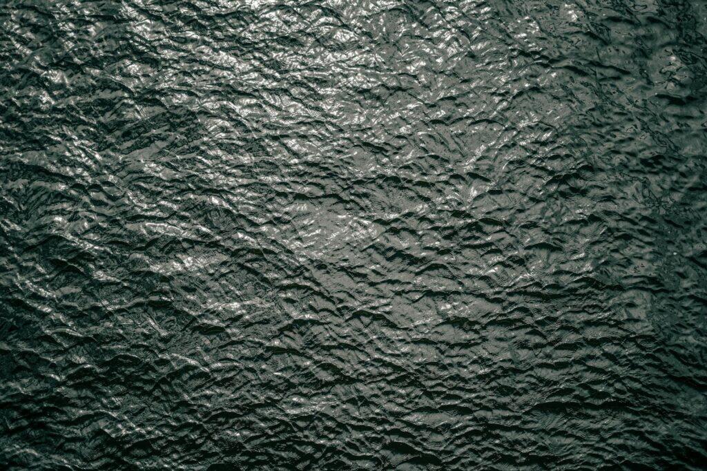 Close-up texture of calm dark green water with gentle ripples, evoking the still, weightless quality of a float session