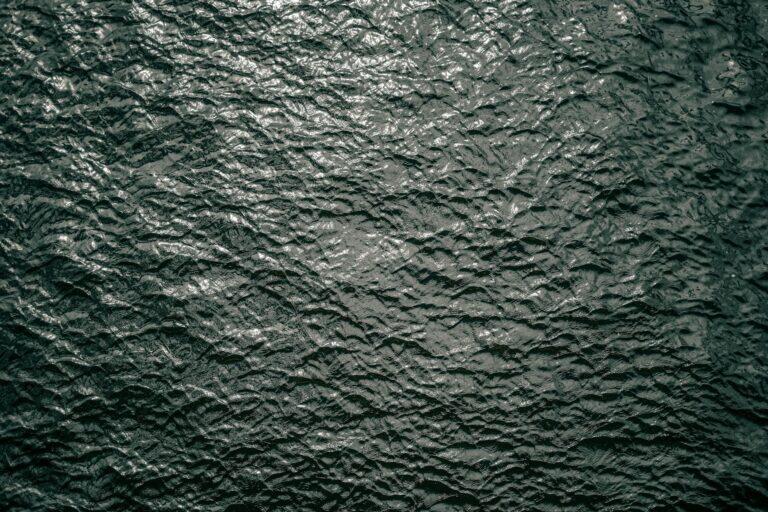 Close-up texture of calm dark green water with gentle ripples, evoking the still, weightless quality of a float session