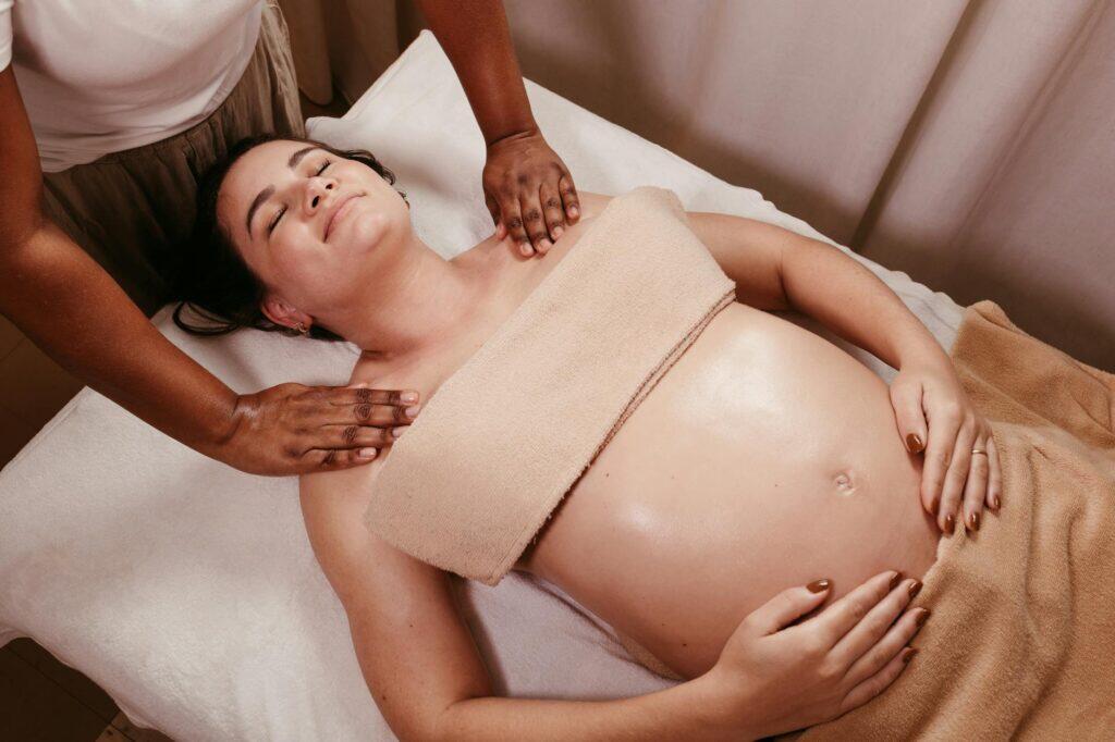 A pregnant woman receiving a calm, professional prenatal massage in a soft-lit spa setting, side-positioned and supported