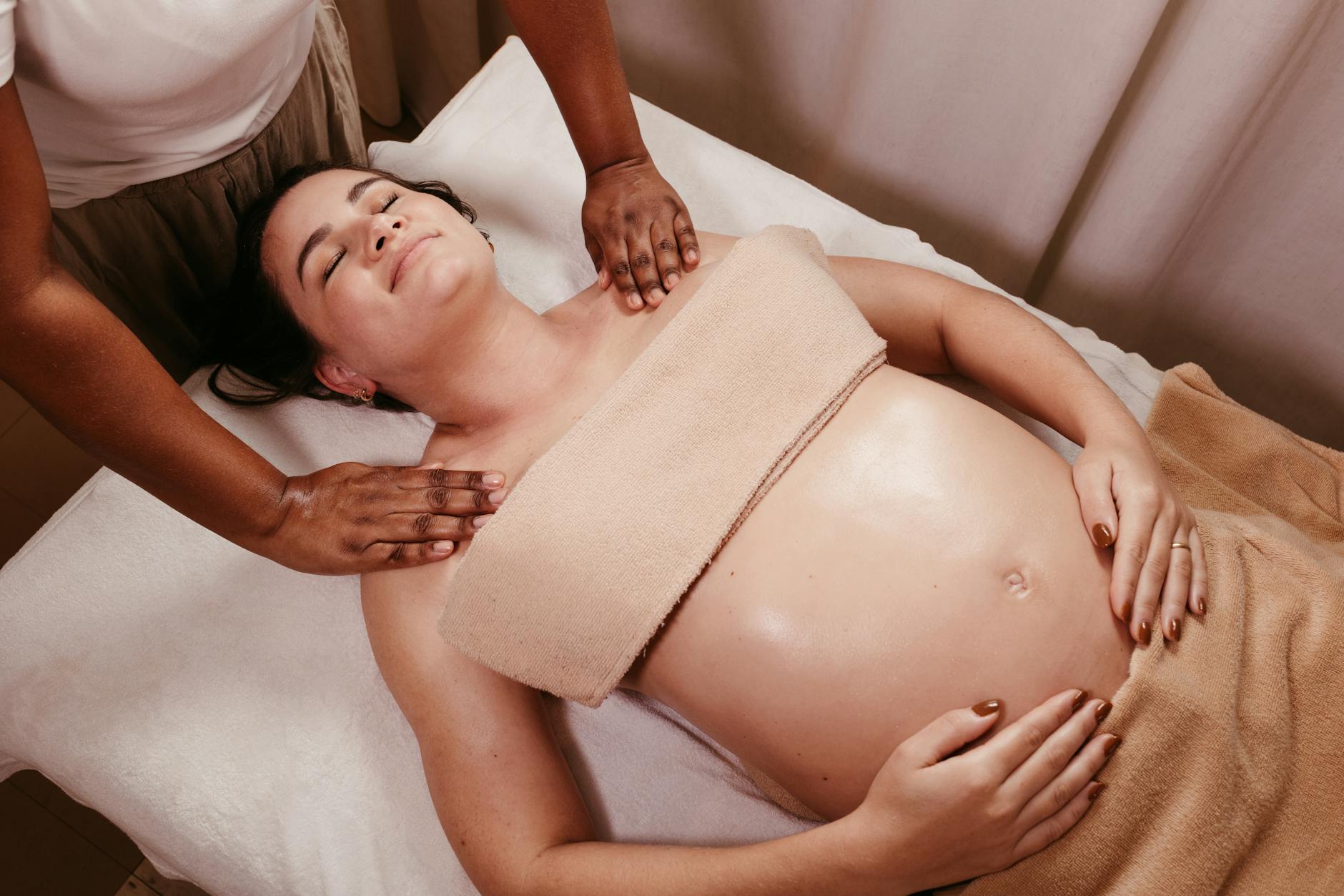 A pregnant woman receiving a calm, professional prenatal massage in a soft-lit spa setting, side-positioned and supported