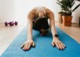 A woman in child's pose on a blue yoga mat in a sunlit home, post-workout recovery and gentle stretch