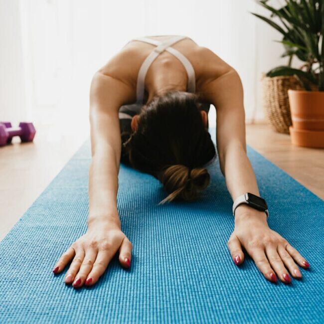 A woman in child's pose on a blue yoga mat in a sunlit home, post-workout recovery and gentle stretch