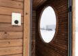Interior view of a modern wooden infrared sauna with a circular window and digital control panel, contemporary Nordic design