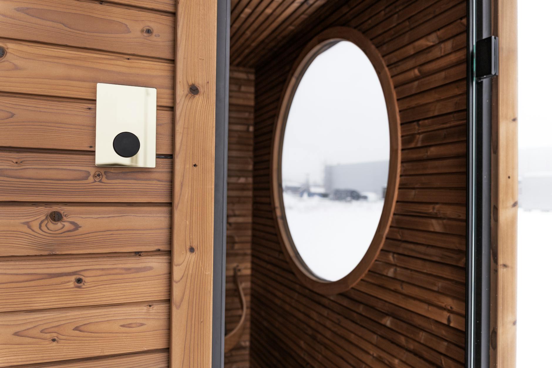 Interior view of a modern wooden infrared sauna with a circular window and digital control panel, contemporary Nordic design