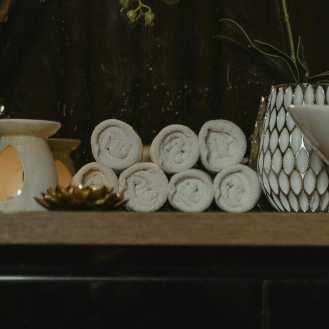 Rolled spa towels with candlelight in a serene treatment setting, evoking the calm of a combined sauna and massage session