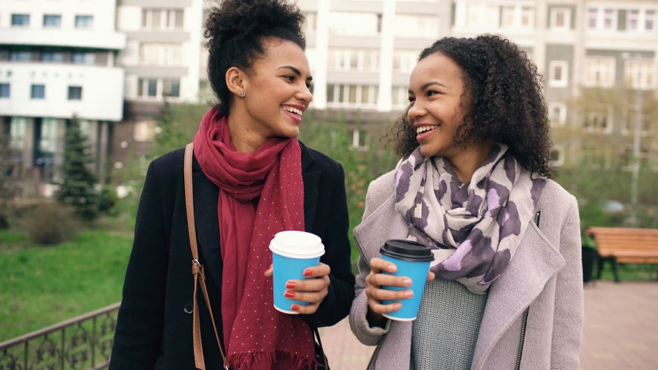 Two friends sitting together on a park bench with takeaway coffees